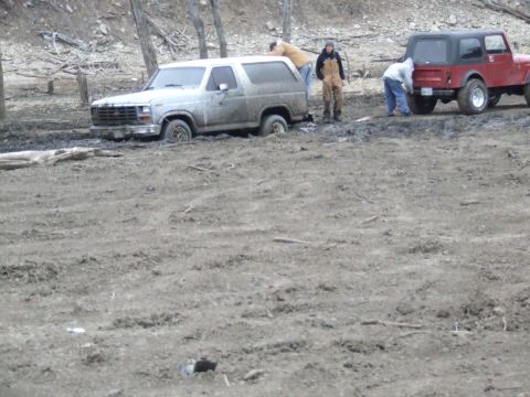 1986 Ford Bronco - A Ford Bronco is stuck in the mud, with a Jeep and several people nearby attempting to assist.