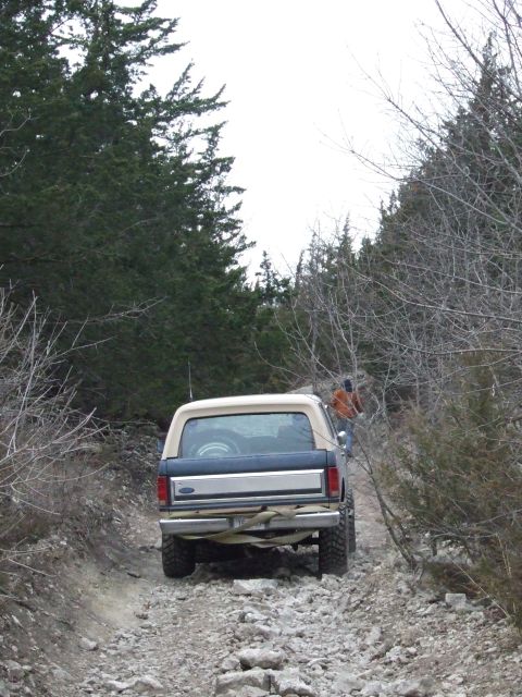 1986 Ford Bronco - A 1986 Ford Bronco navigates a rough, rocky path through a wooded area.