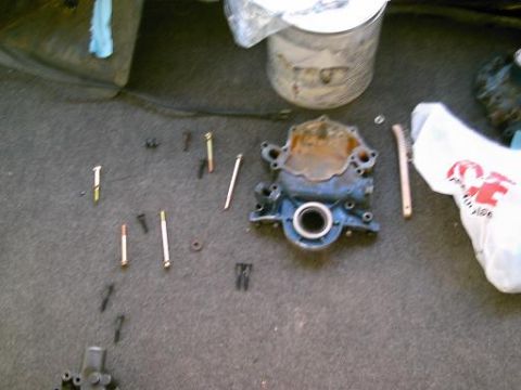 1986 Ford Bronco - Disassembled engine part and hardware laid out on a carpeted floor.