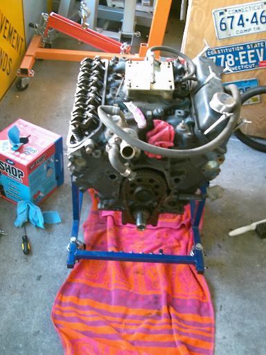 1986 Ford Bronco - Engine assembly on a stand, with tools and license plates in the background.