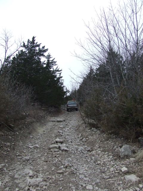 1986 Ford Bronco - A 1986 Ford Bronco navigates a rough, rocky path through a wooded area.