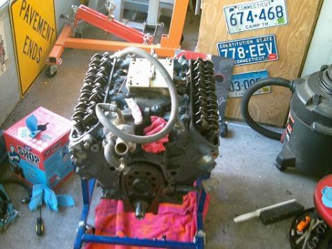 1986 Ford Bronco - Engine on a stand with shop supplies and license plates visible in the background.