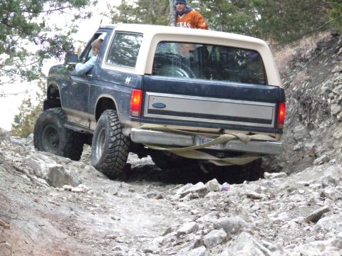 1986 Ford Bronco - A Ford Bronco with off-road tires is driven over a challenging rocky terrain.
