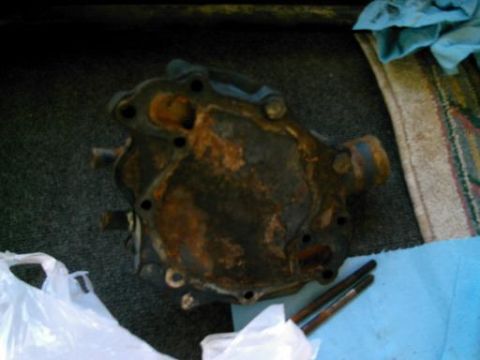 1986 Ford Bronco - A heavily rusted engine part sits on a surface next to some bolts and a blue cloth.