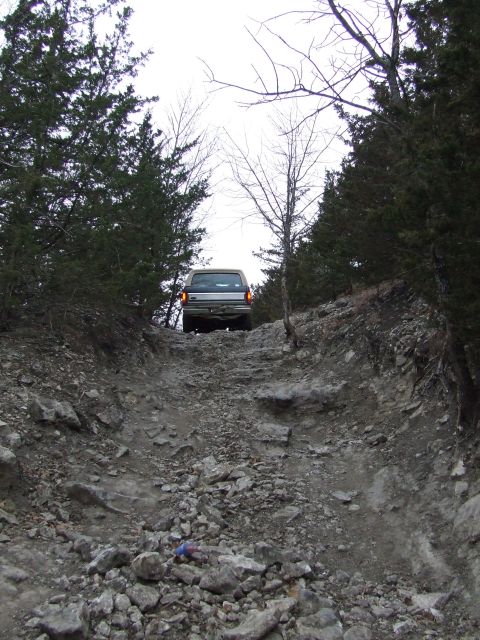 1986 Ford Bronco - A vehicle navigates a challenging off-road path through a wooded area.