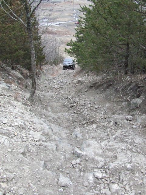 1986 Ford Bronco - A 1986 Ford Bronco navigates a challenging rocky incline surrounded by trees.