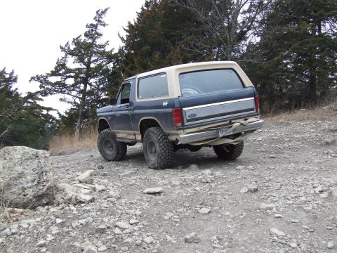 1986 Ford Bronco - This Ford Bronco is navigating a rough, rocky terrain with trees in the background.