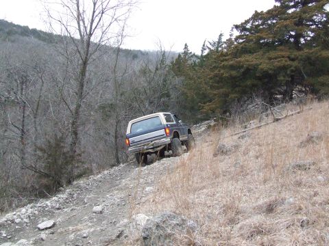 1986 Ford Bronco - A blue and white Ford Bronco navigates a challenging off-road trail.