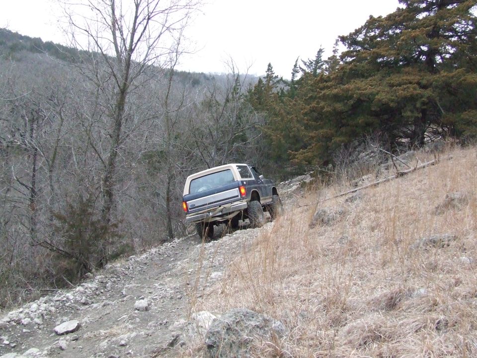Blue and white Ford Bronco driving up a rocky, wooded hill