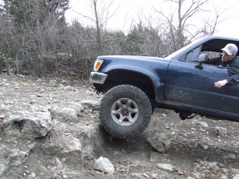 1986 Ford Bronco - Driver maneuvers a blue pickup truck over rough, rocky ground during an off-road excursion.