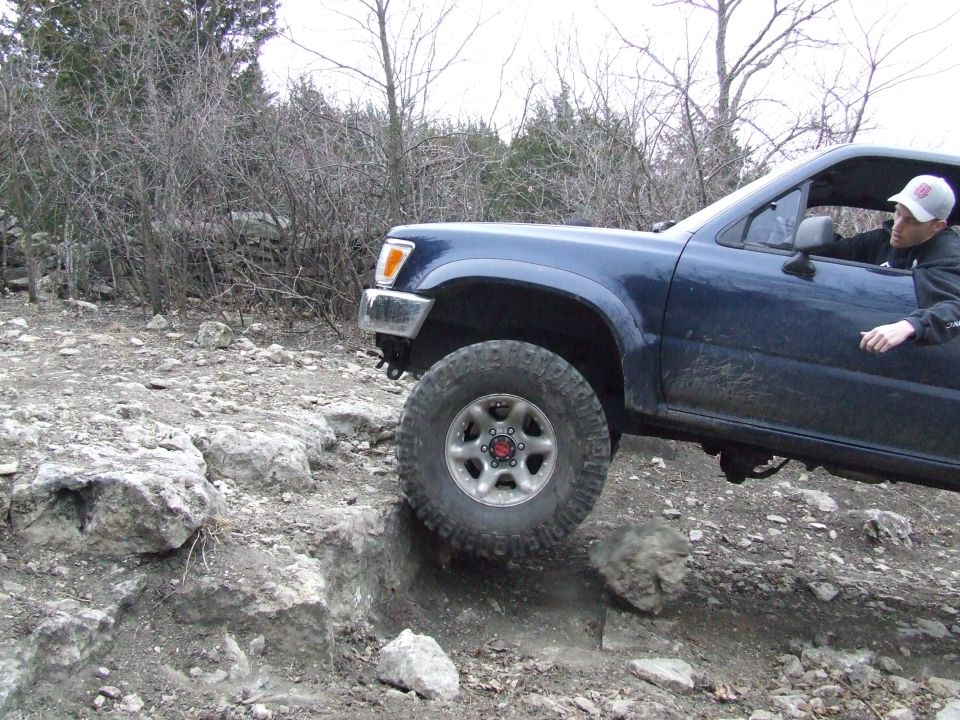 Blue pickup truck with aftermarket wheels navigating rocky terrain