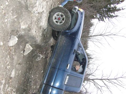 1986 Ford Bronco - A blue pickup truck navigates a rocky off-road trail with its front passenger wheel elevated.