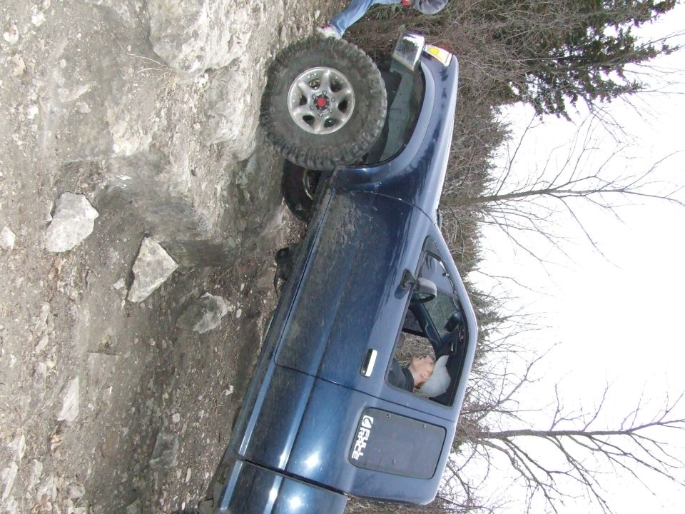 Blue pickup truck with one wheel up on rocks, driver inside