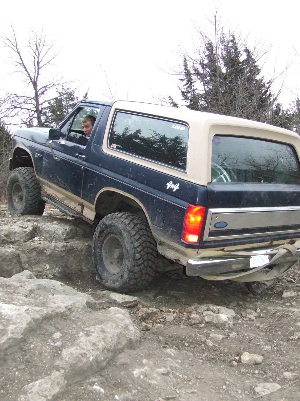 Dark blue Ford Bronco with tan top navigating rocky terrain, driver visible