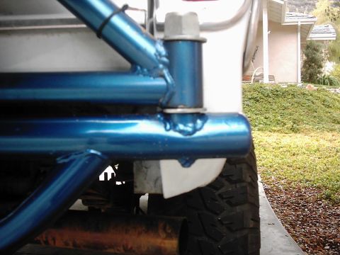 1978 Ford Bronco - Close-up of a blue roll cage mounted to the rear of a white vehicle, with a tire and exhaust visible.