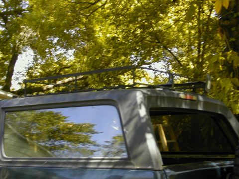 1993 Ford Bronco - Low upward shot of a fabricated steel roof rack mounted on the hardtop of a dark blue-green SUV, framed against sunlit tree canopy. The rac…