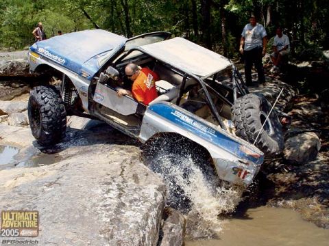 1991 Ford Bronco - This heavily modified off-road vehicle navigates a challenging water and rock obstacle during an event.