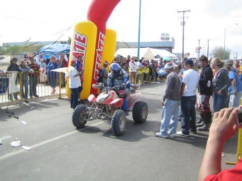 1990 Ford Bronco - racer on a red Honda quad rides under a yellow Tecate inflatable arch as spectators line the course.