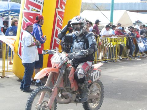 1990 Ford Bronco - dirt bike racer on number 202 raises a hand in salute while riding past a barricaded crowd at the race.