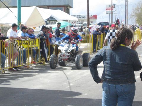 Blue and white ATV quad racer on course as a woman waves