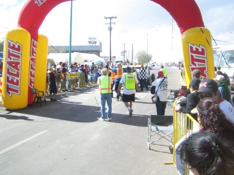 Spectators walking under a large red and yellow Tecate inflatable arch