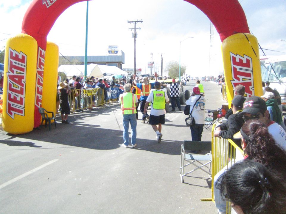 Spectators walking under a large red and yellow Tecate inflatable arch