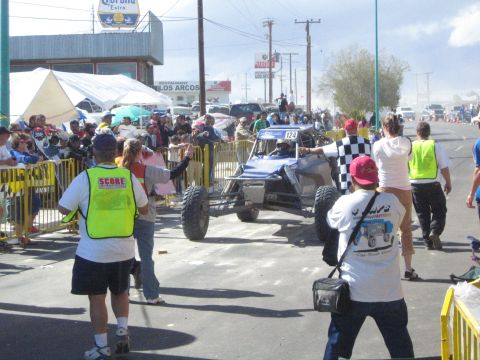 Blue open off-road race buggy number 124 passing a checkered flag