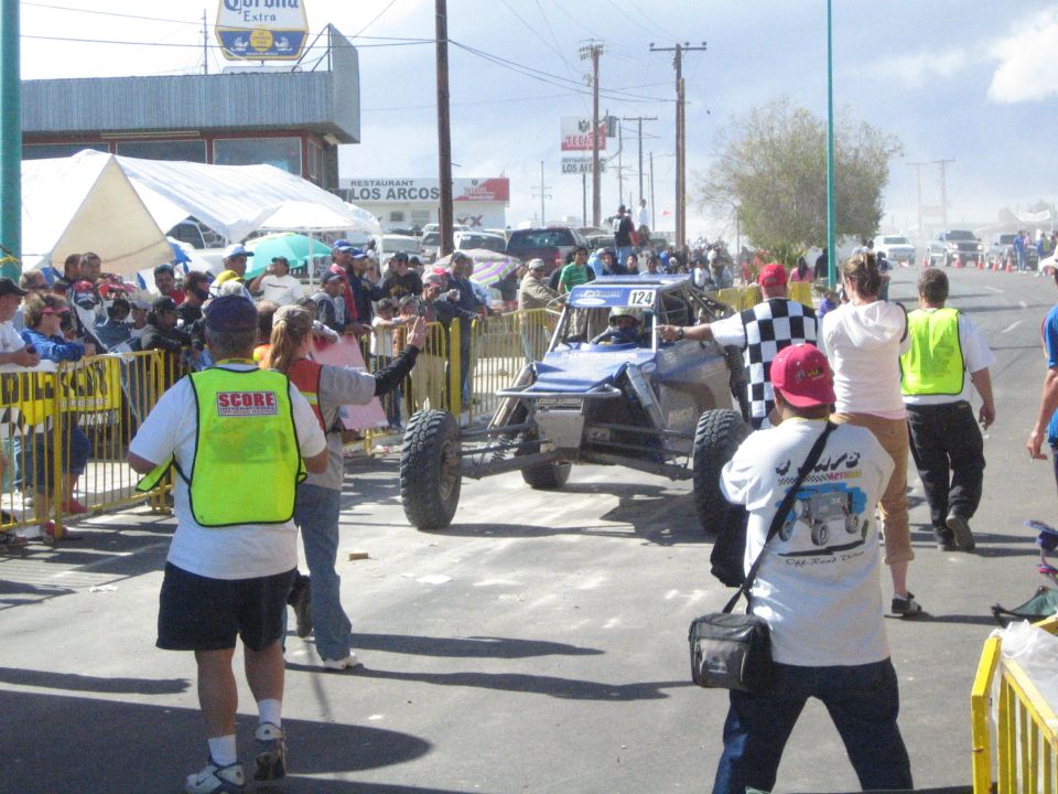 Blue open off-road race buggy number 124 passing a checkered flag