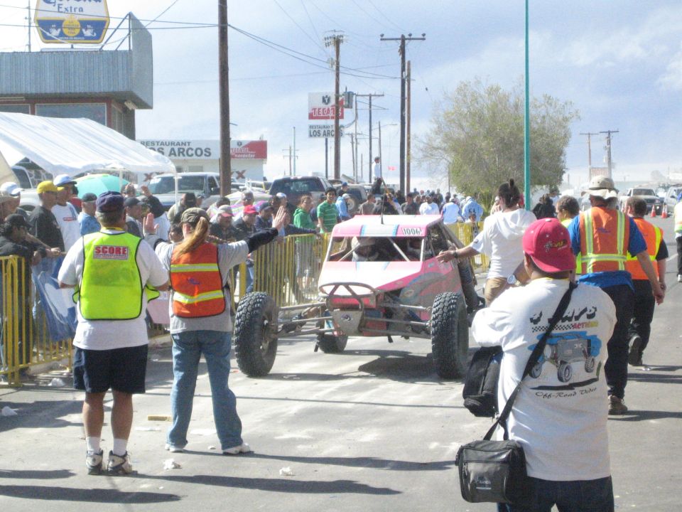 Pink and white off-road race buggy among officials waving people on