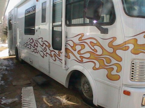 1977 Ford F-250 - A white motorhome is parked outdoors, prominent flame graphics along its side.