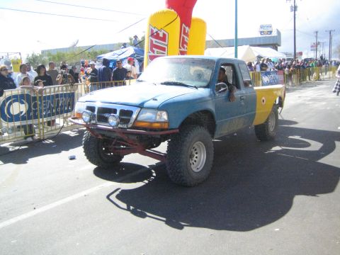 Blue and yellow off-road pickup truck on a paved street at a desert race event