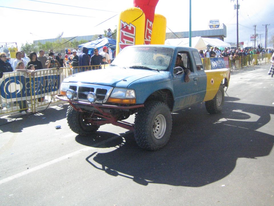 Blue and yellow off-road pickup truck on a paved street at a desert race event