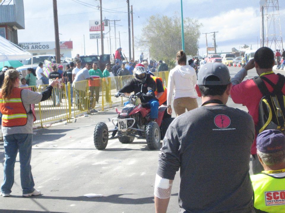 Rider on a red racing ATV moving down a street lined with spectators