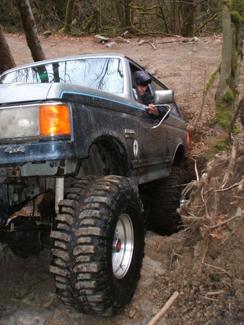 1987 Ford Bronco - This lifted 1987 Ford Bronco tackles a challenging off-road trail with large tires and a driver focused on the path ahead.