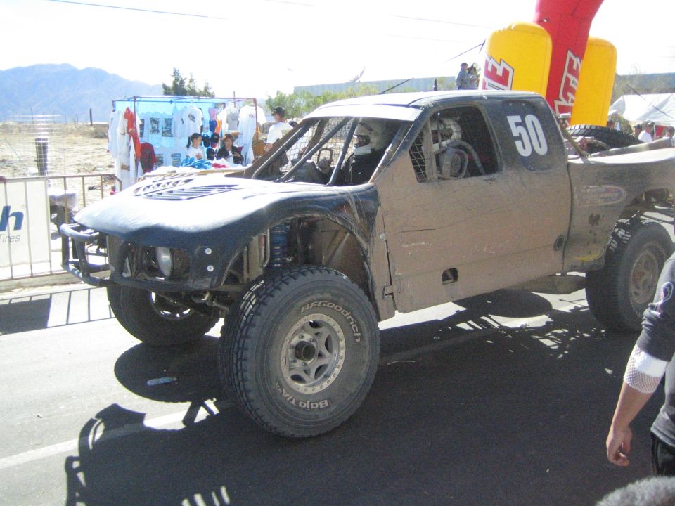 Mud-covered white off-road race truck number 50 parked at a race event