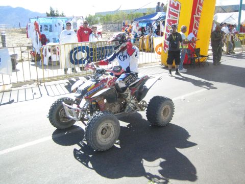 Rider on a white racing ATV on a street with spectators and a Tecate arch