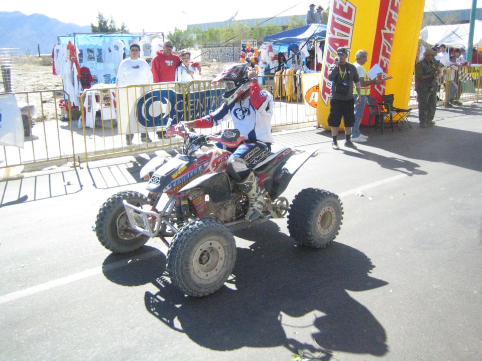 Rider on a white racing ATV on a street with spectators and a Tecate arch