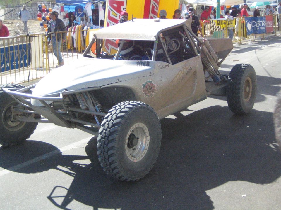 Silver tube-frame off-road race buggy on a paved street at an event