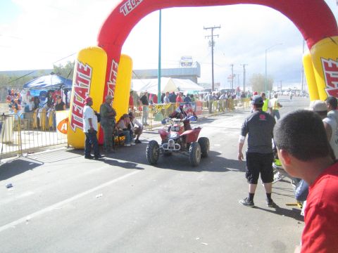 Racing ATV parked under a Tecate arch on a street lined with spectators