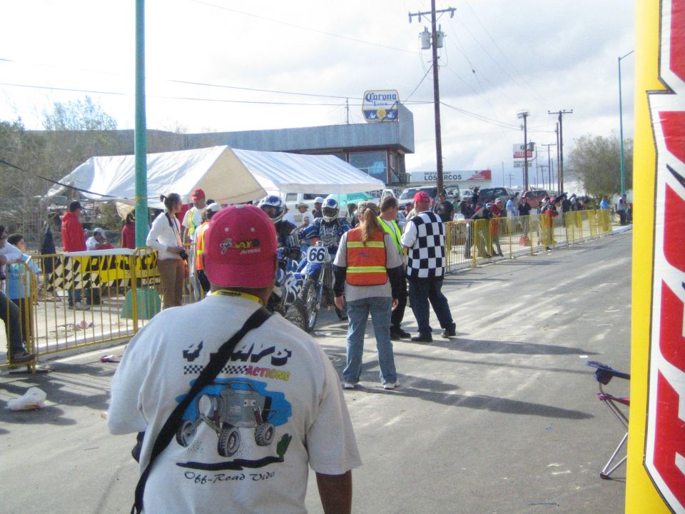 Spectators and dirt bikes at a street staging area for an off-road race