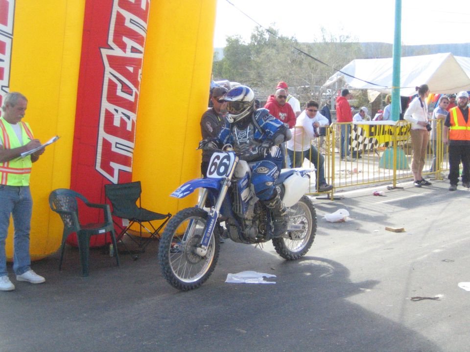 Rider on a blue dirt bike number 66 beside a Tecate arch on pavement