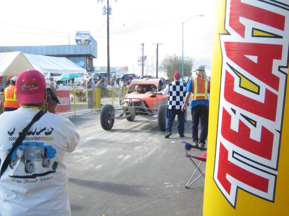 Spectators photographing an orange race buggy at a street start area