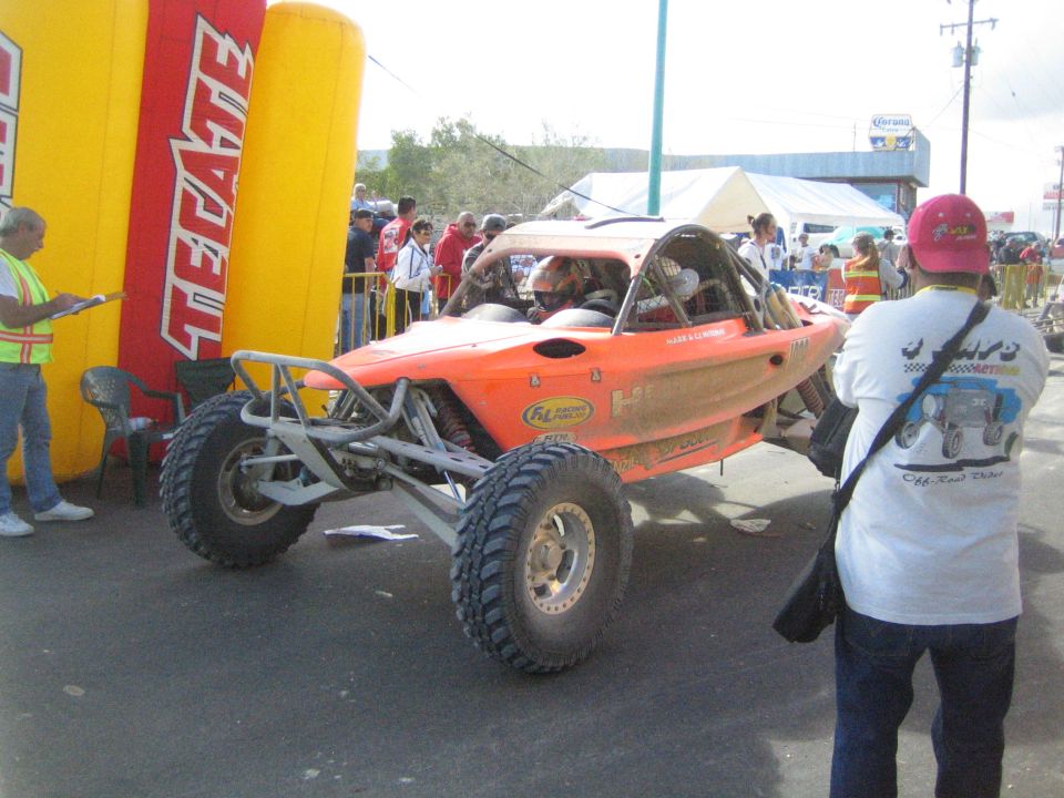 Orange tube-frame off-road race buggy on a street with spectators