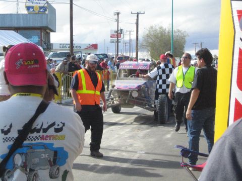 Officials and crowd around a purple race buggy on a street