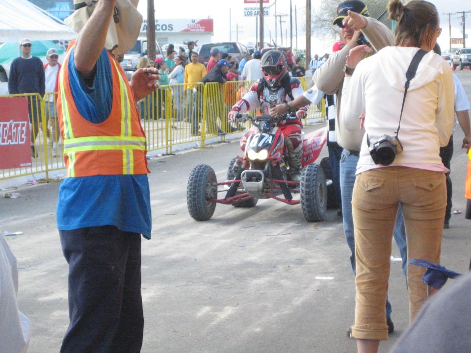 Helmeted rider on a red racing ATV approaching officials on a street