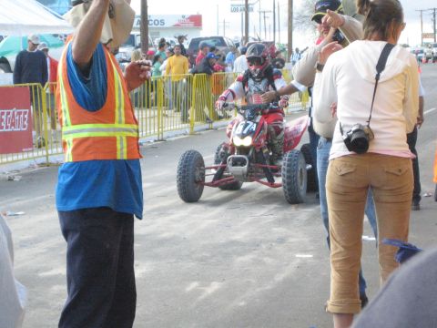 Rider on a red racing ATV number 7A on a street with officials nearby