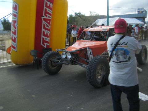 Orange tube-frame race buggy number 1000 beside a Tecate arch on a street