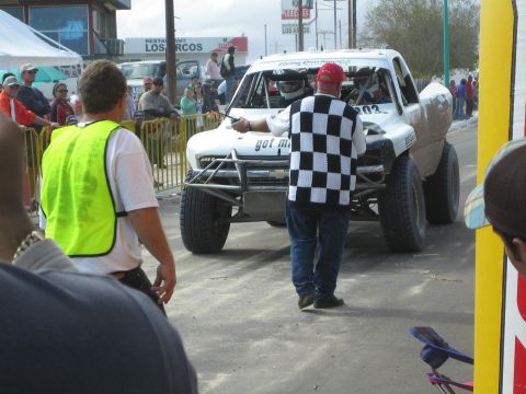 White off-road race truck at start line, official with checkered flag and spectators