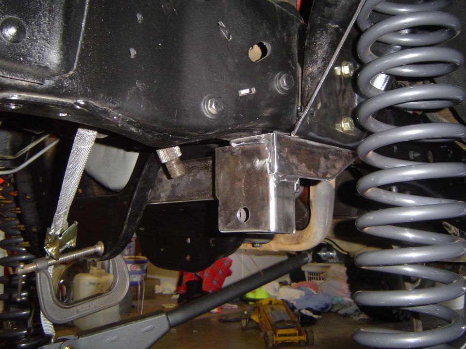 Fabricated bare-steel suspension bracket welded to frame rail beside gray coil spring