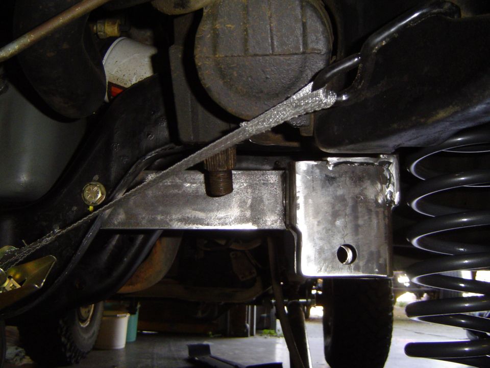 Freshly welded bare steel suspension brackets on a truck frame with coil spring at right